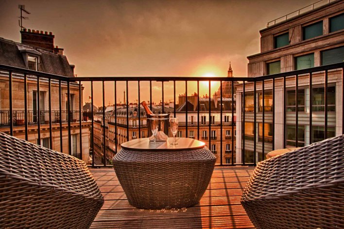 Terrasse parisienne avec soleil couchant, équipée de fauteuils et coupes de champagne