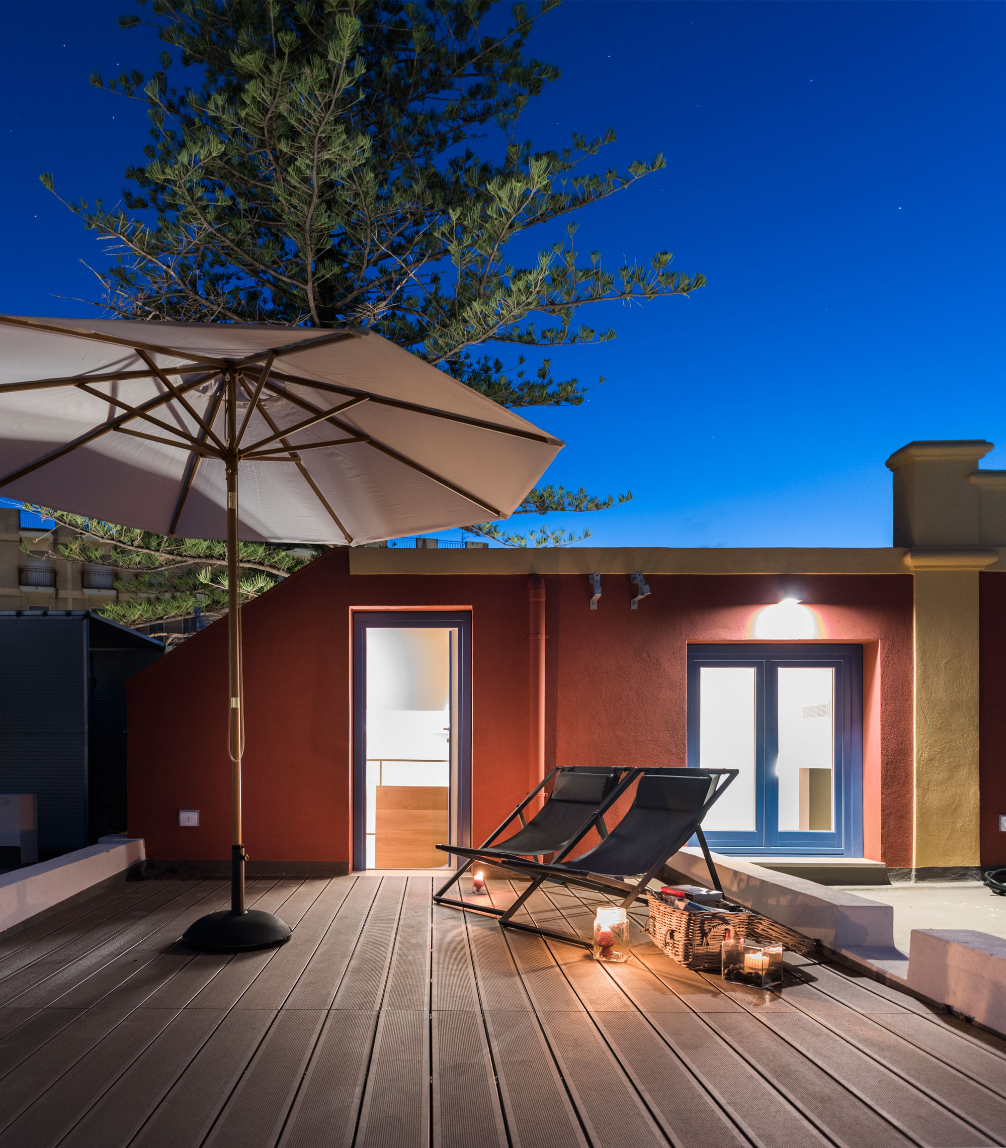 Terrasse en bois abritée d'un parasol sur laquelle sont posées 2 transats, vue de nuit