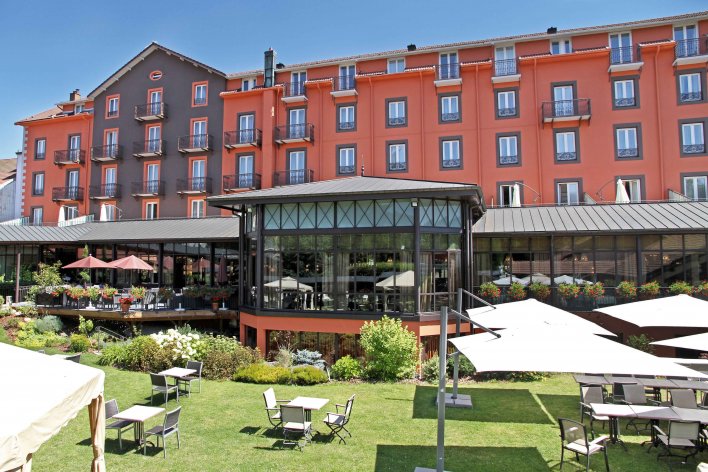 Façade rouge et noire du Grand Hôtel & Spa de Gérardmer, devant la verrière ouverte sur le jardin de l'établissement