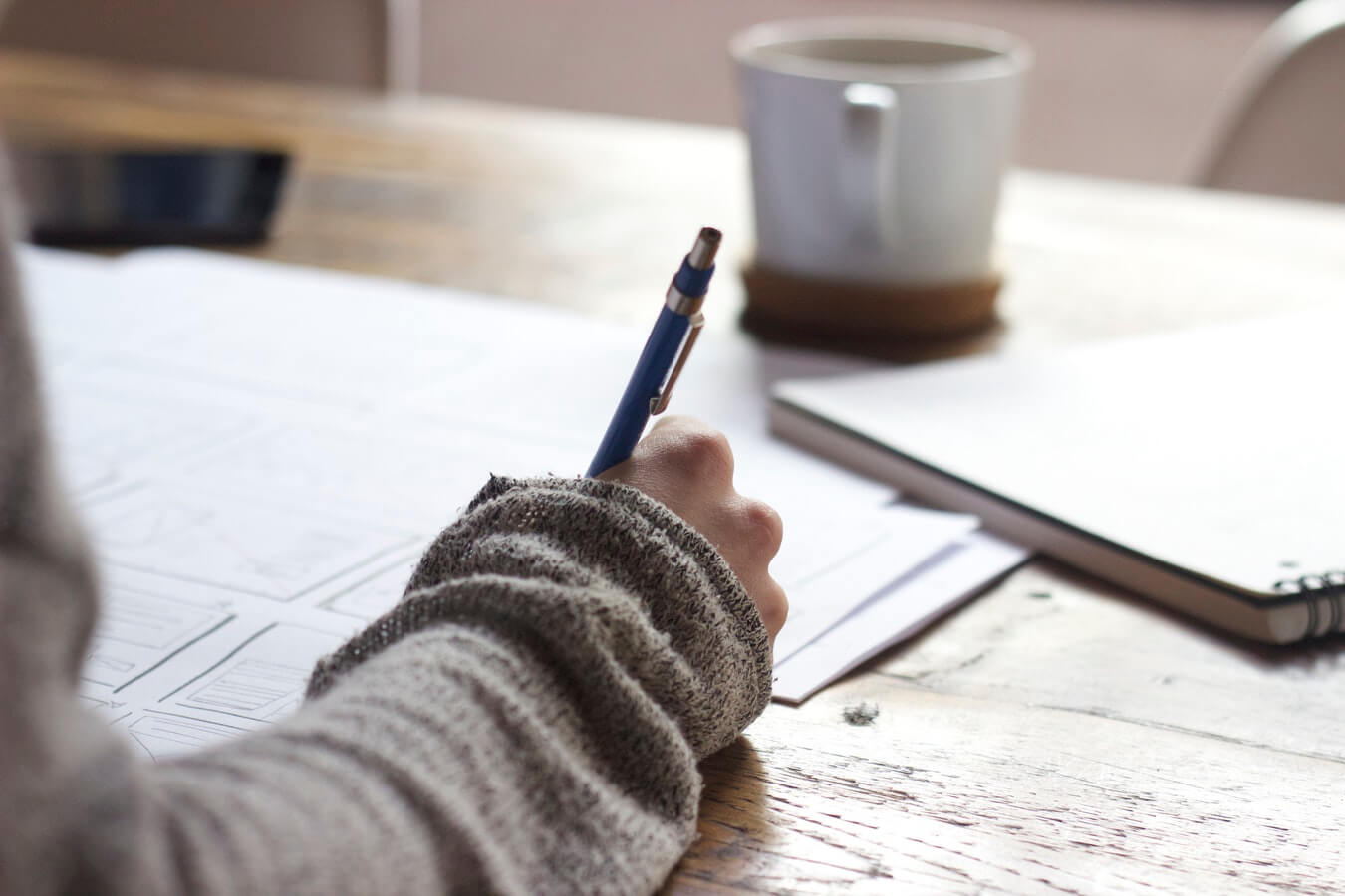 gros plan sur une main droite tenant un stylo bille sur une table en bois