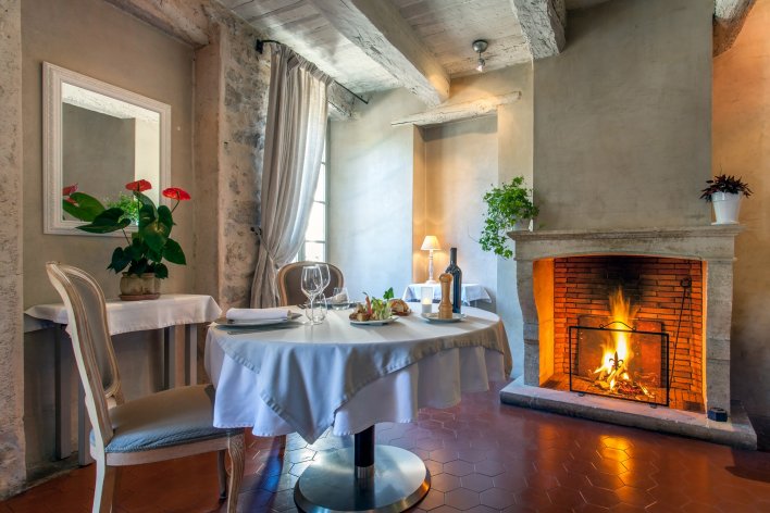 Table ronde dressée pour un couple d'amoureux dans une pièce avec poutres apparentes et feu de cheminée allumé