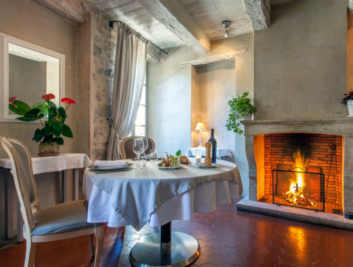 Table ronde dressée pour un couple d'amoureux dans une pièce avec poutres apparentes et feu de cheminée allumé