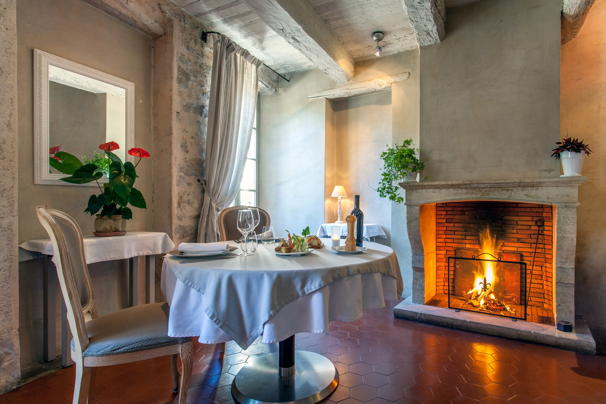 Table ronde dressée pour un couple d'amoureux dans une pièce avec poutres apparentes et feu de cheminée allumé