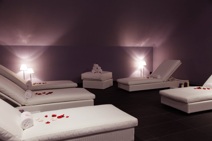 Salle de soins spa équipée de tables de massage parsemées de pétales de roses dans une ambiance tamisée