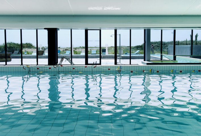 Vaste piscine intérieure avec baie vitrée accédant sur une terrasse extérieure