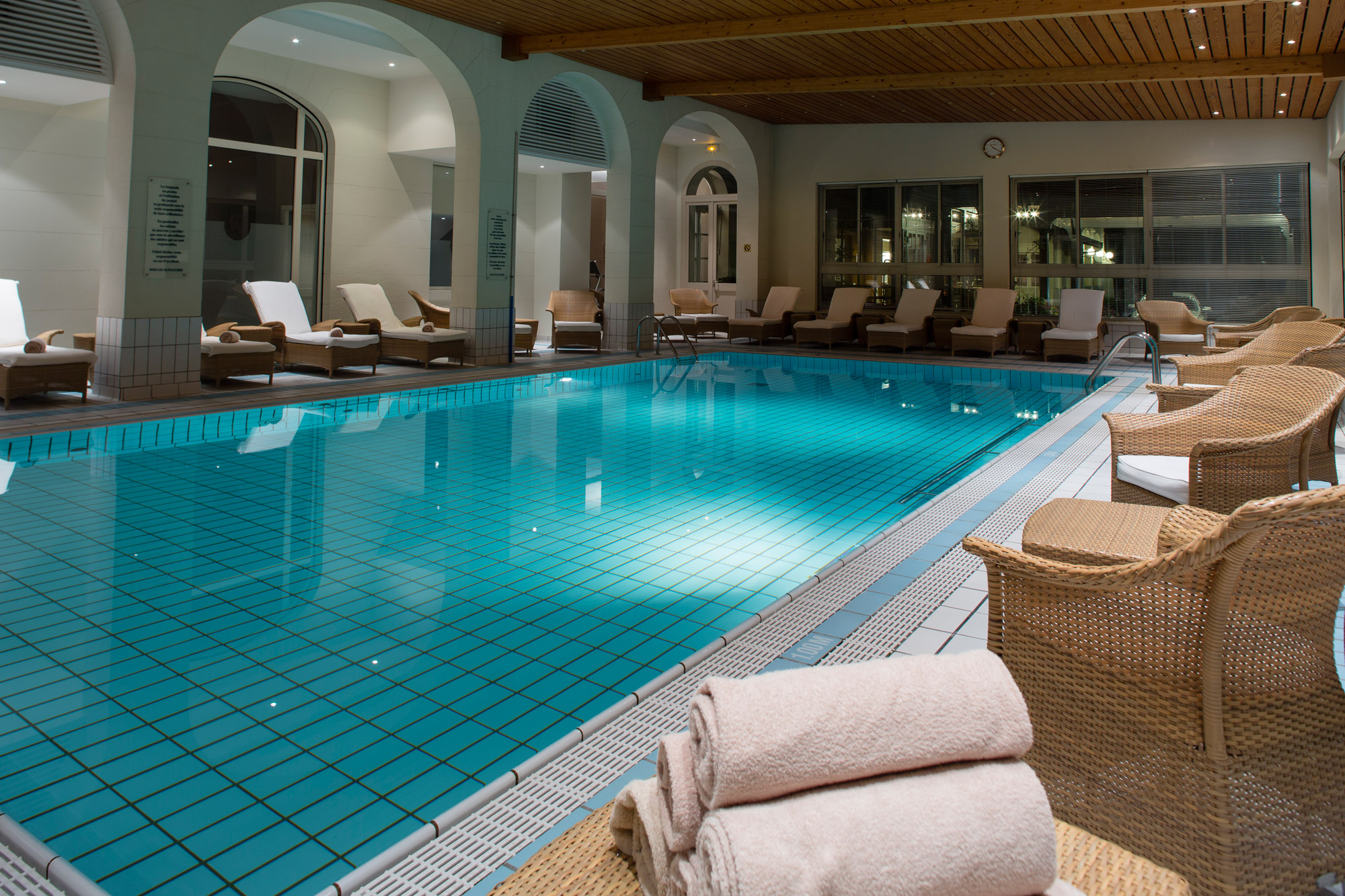 Vaste piscine intérieure entourée de tranats et de fauteuils pour se relaxer.