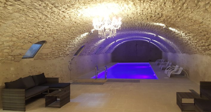 Piscine intérieure installée dans une cave voûtée, surplombée d'un lustre, avec canapés tout autour pour se relaxer.