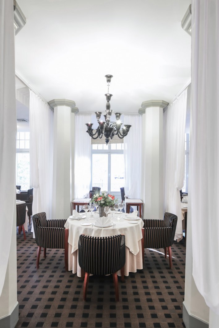 Aperçu d'une salle de restaurant avec tables dressées dans un cadre chic avec colonnes, drapés et lustres.