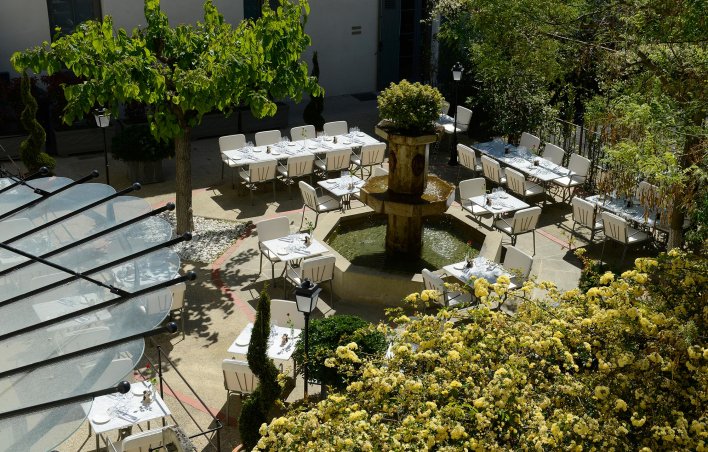 Terrasse provençale avec fontaine centrale et tables pour déjeuner tout autour.