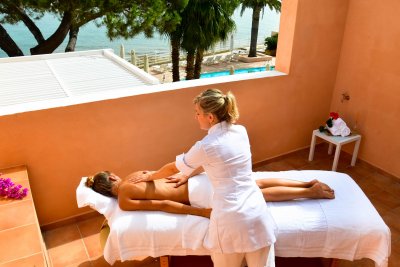 Jeune femme installée sur une table de massage sur un balcon de chambre d'hôtel, en train de recevoir un soin.