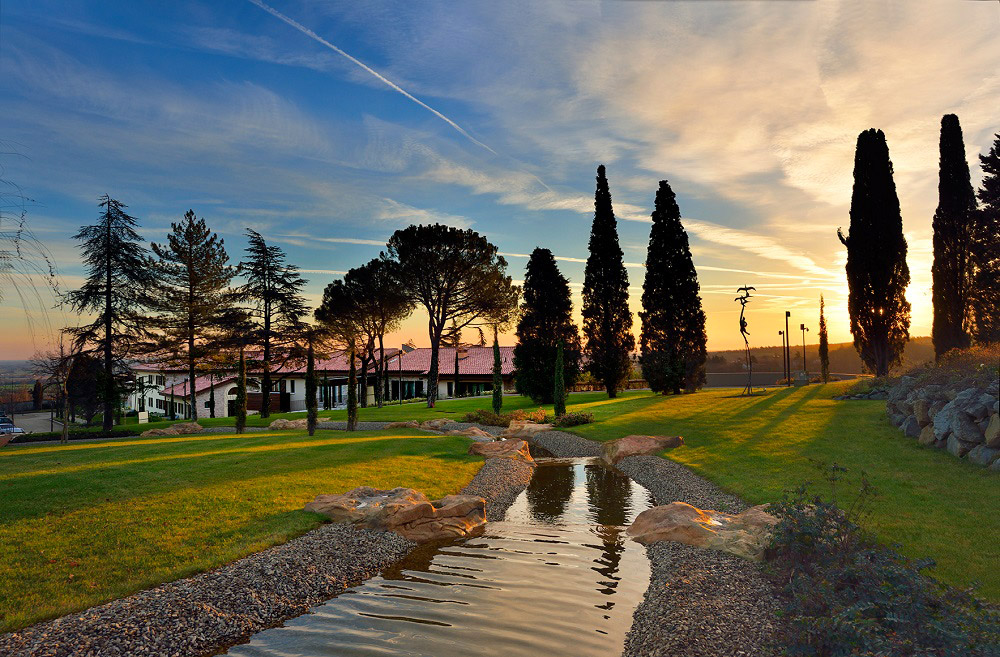 Vaste parc arboré en Italie avec cours d'eau traversant la propriété au coucher du soleil.