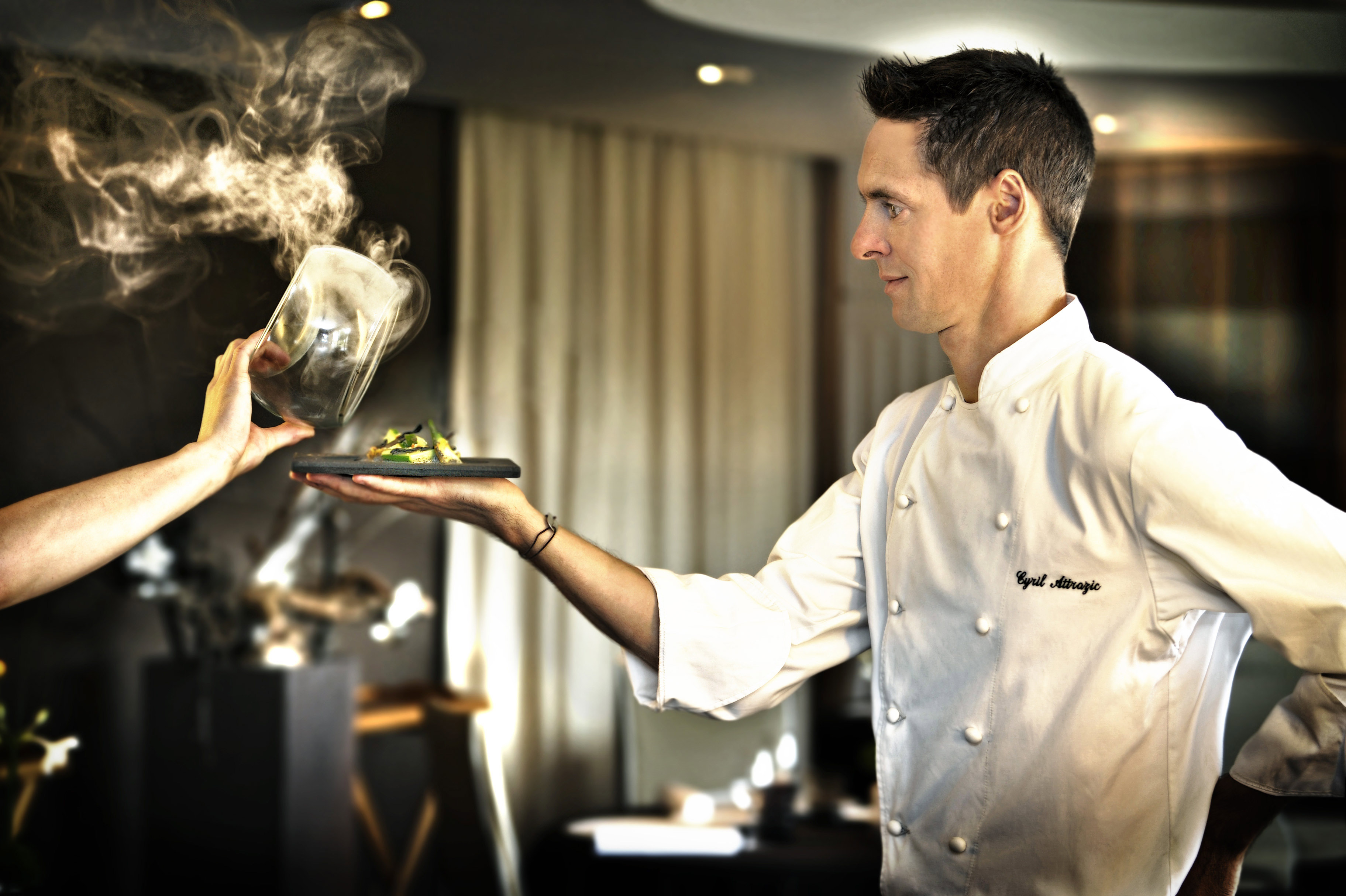 Chef en veste de cuisine de profil avec un plat dans la main