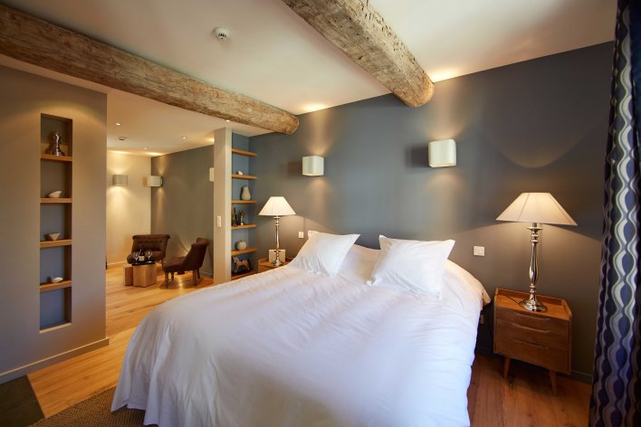 Chambre lit double, linge de lit blanc, murs gris, poutres apparentes