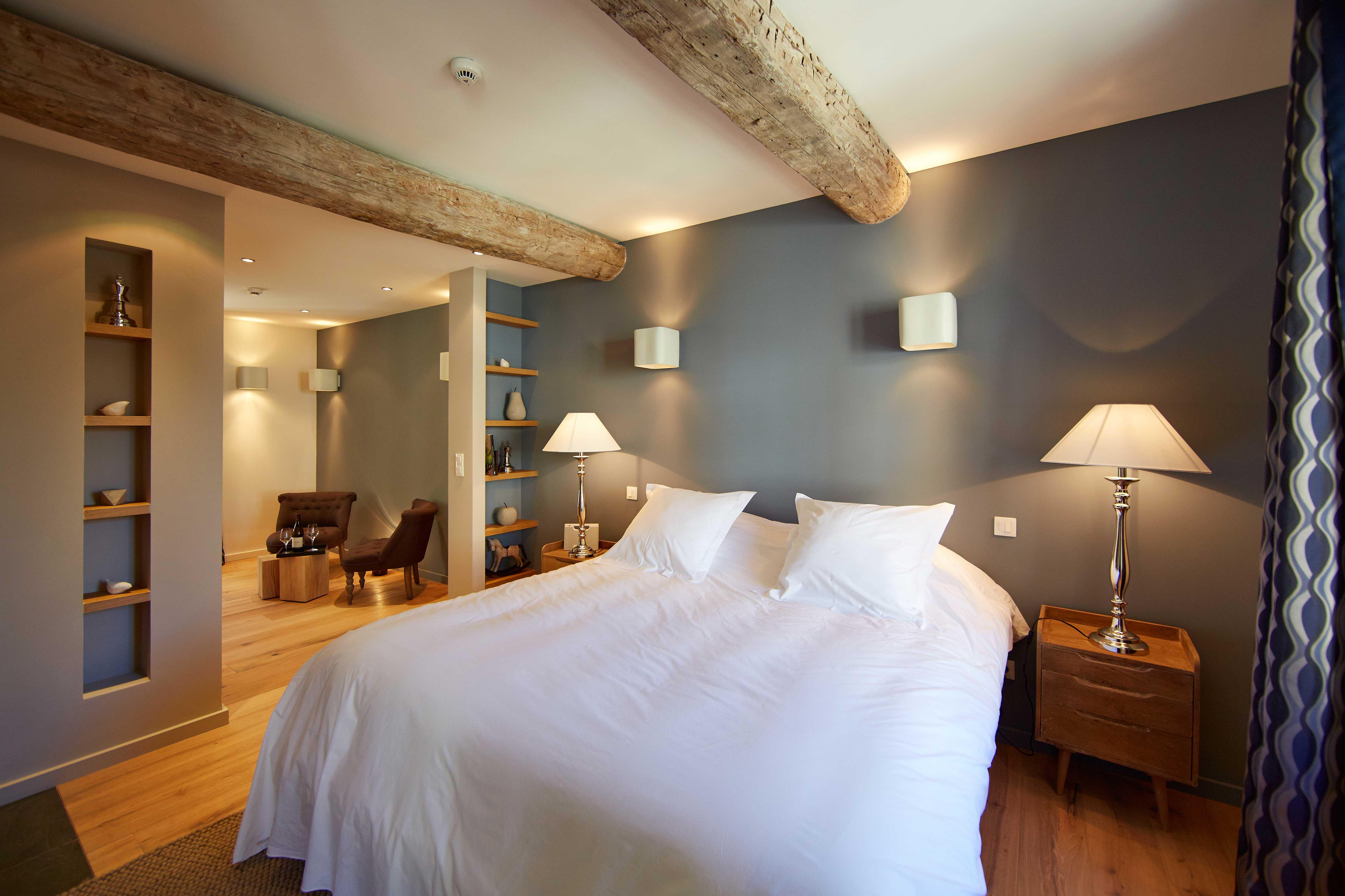 Chambre lit double, linge de lit blanc, murs gris, poutres apparentes