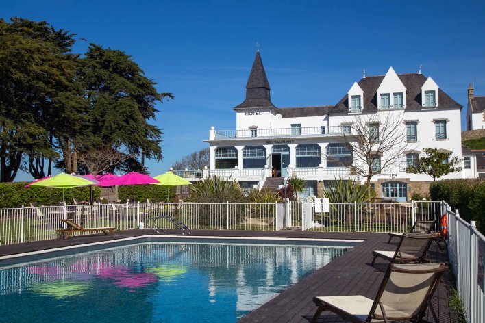 Grande piscine avec transat, devant grand hôtel avec restaurant
