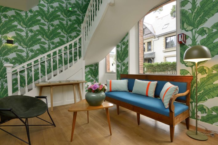Hall avec escalier blanc en angle, canapé vintage bleu velours et bois, éléments décoratifs style scandinave