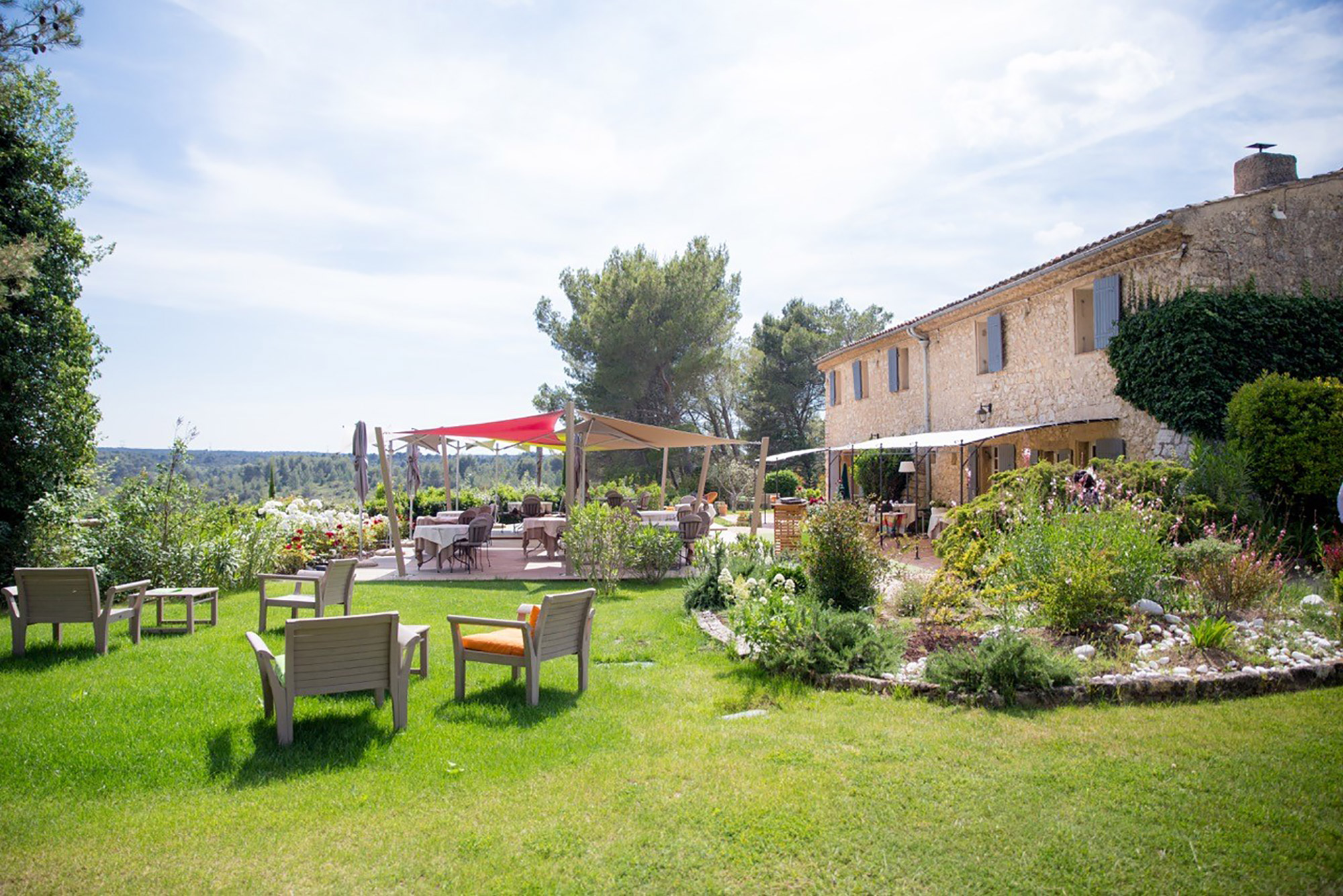 Jardin avec mobilier en bois, large pelouse et terrasse couverte à côté d'un Mas provençal