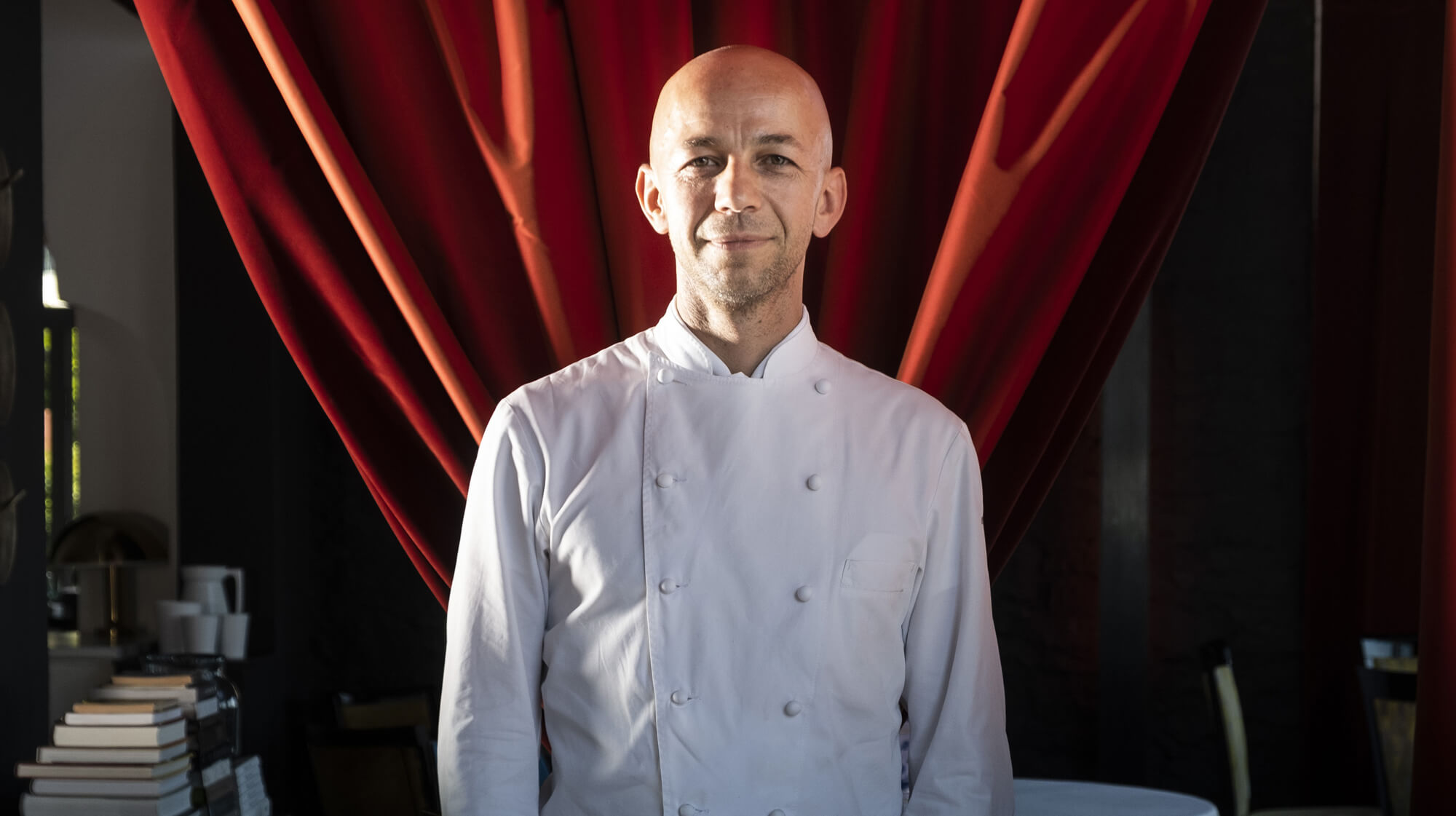 Portrait d'un chef en veste de cuisine avec en arrière plan un rideau rouge en velours