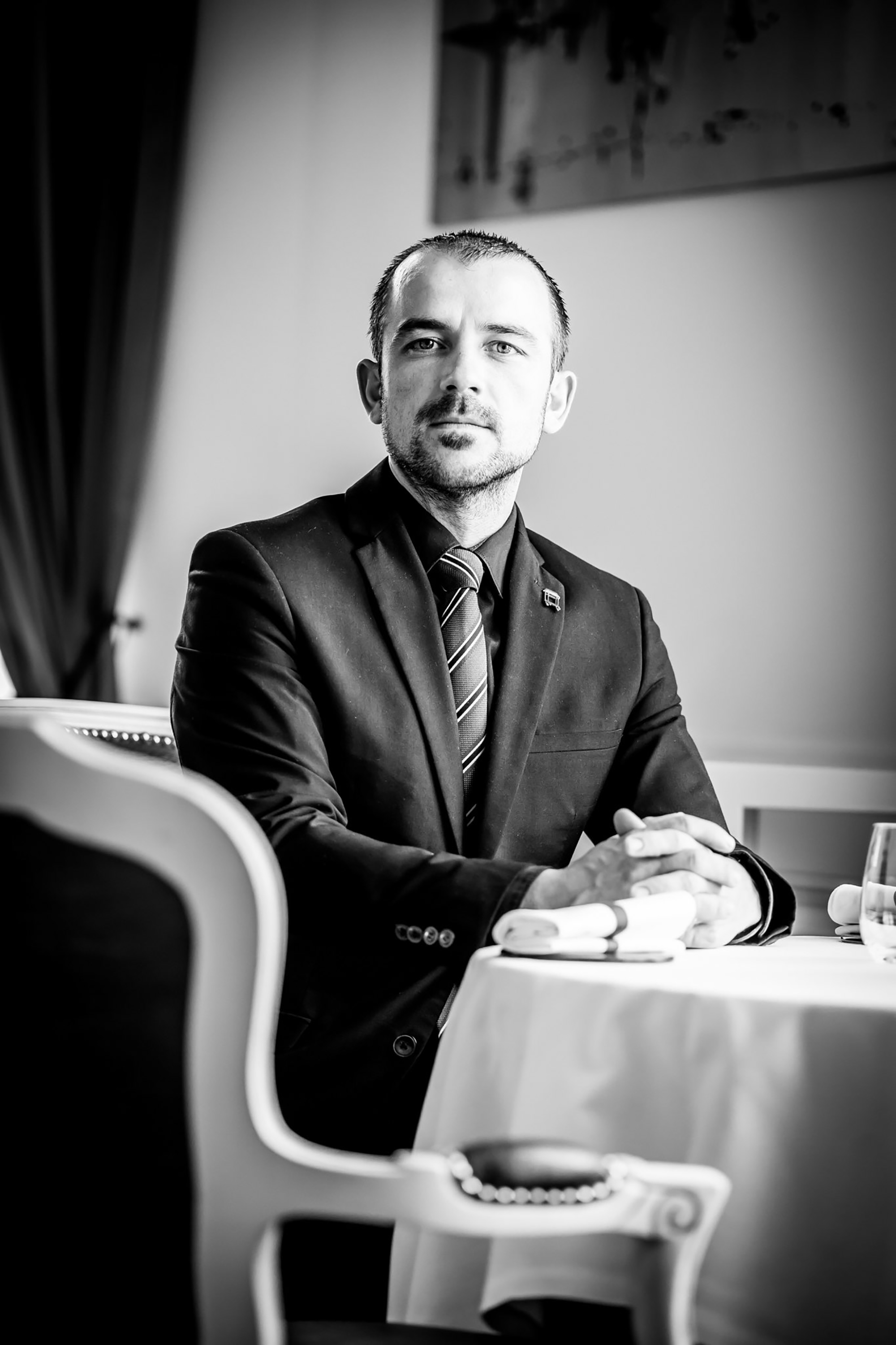 Protrait noir et blanc d'un homme assis sur une chaise devant une table nappée