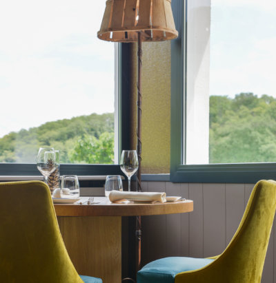 chaises bleu et jaune en velour, table en bois et grandes fenêtres