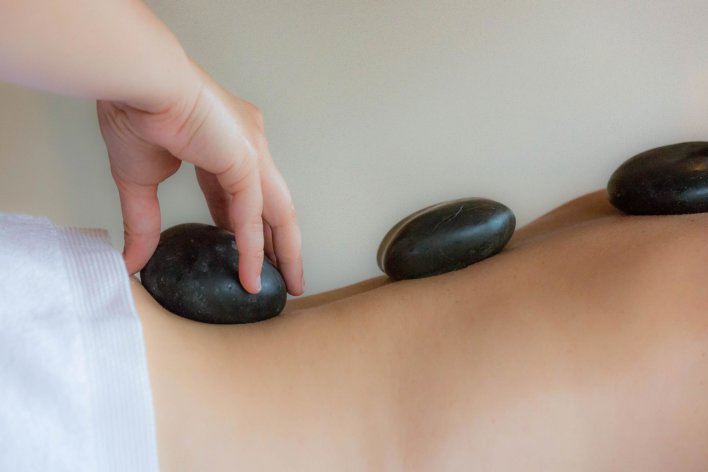 dos nus et serviette à la taille, une main pose des pierres noires le long de la colonne vertébrale