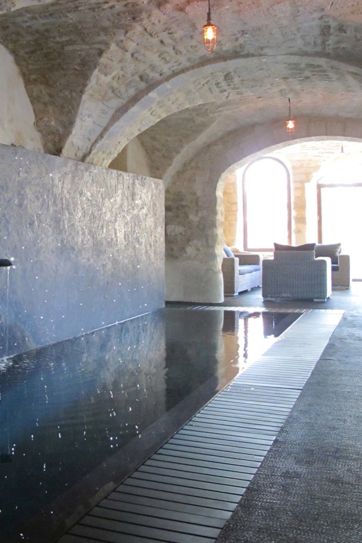 Piscine intérieure sous voute donnant sur une grande baie vitrée avec espace détente et meuble en rotin