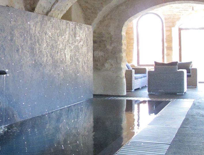 Piscine intérieure sous voute donnant sur une grande baie vitrée avec espace détente et meuble en rotin