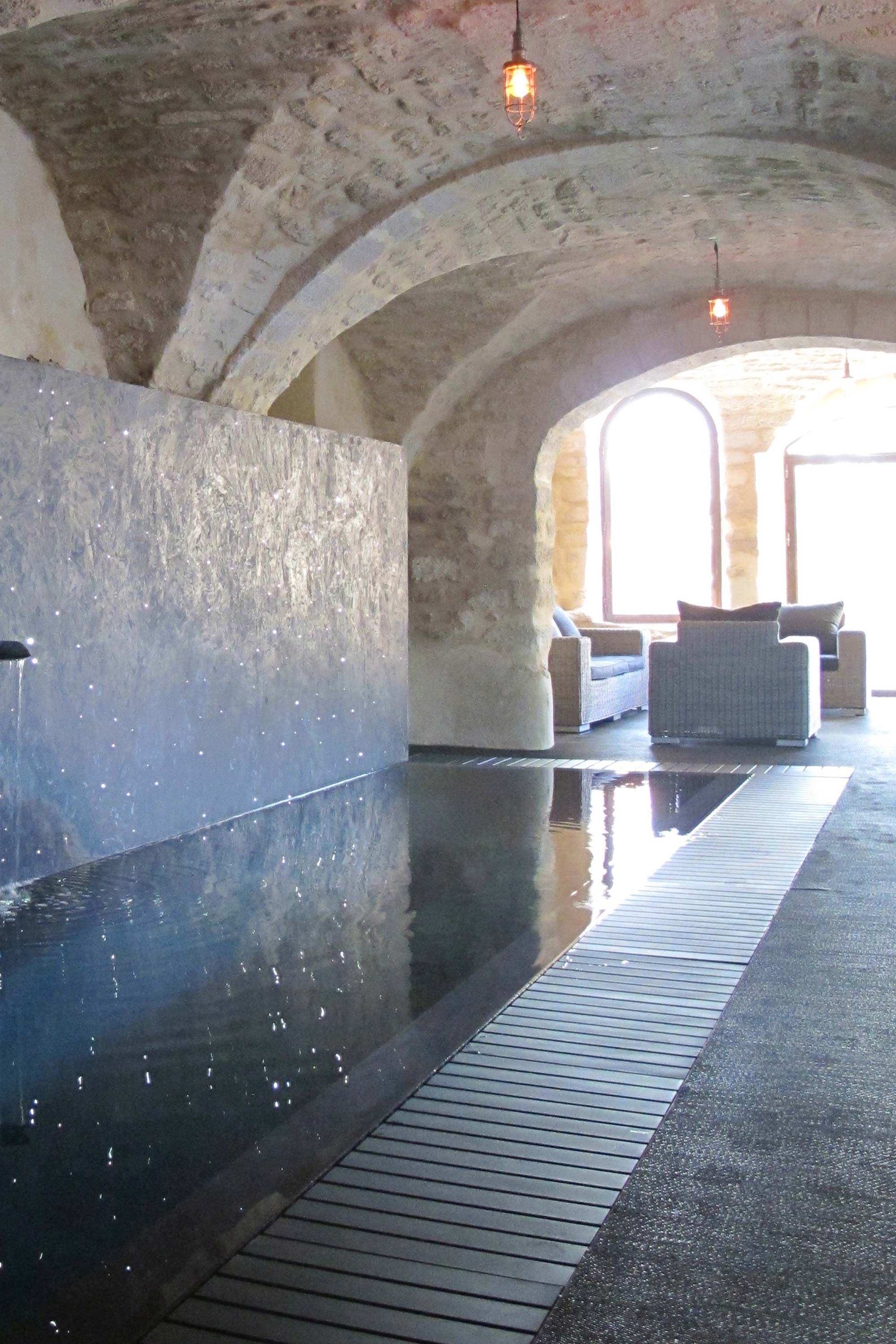Piscine intérieure sous voute donnant sur une grande baie vitrée avec espace détente et meuble en rotin