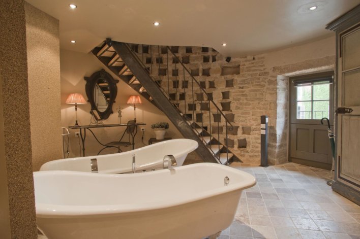 Pièce ronde de salle de bain avec double baignoire, escalier longeant le mur, porte vitrée sur l'extérieur