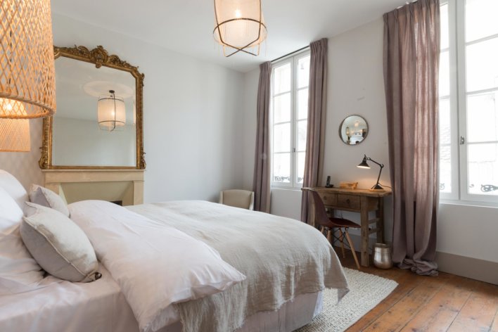 Chambre lit double, détail suspension en rotin illuminée, lumière tamisée, quelques miroirs en décoration et linge de lit couleur lin et ivoire