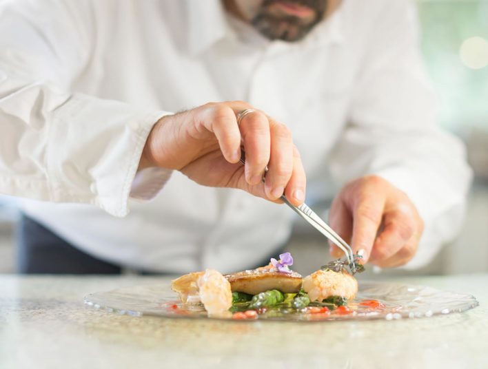 détail sur mains d'un chef dressant une assiette avec une petite pince de précision