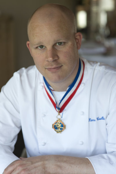 Photo portrait d'un chef en veste de cuisinier blanche, décoré du col bleu blanc rouge de Meilleur ouvrier de France, veste brodée bleue au nom du chef, soit Pierre Caillet