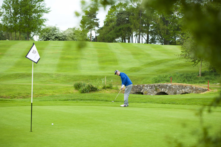 Golfeur en polo bleu, vue de profil, tenant son club de golf dans les deux mains prêt à tirer dans une balle