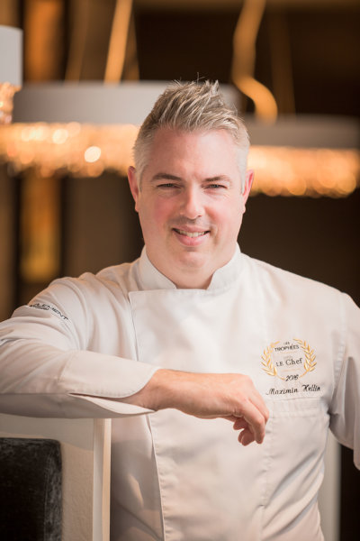 Chef debout, accoudé à un tableau ardoise, vêtu d'une veste de cuisinier blanche