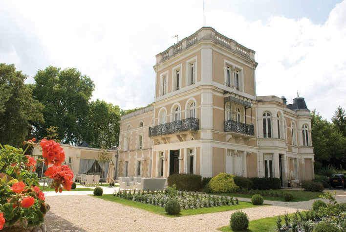 Façade d'hôtel bordé d'un jardin verdoyant à la française.