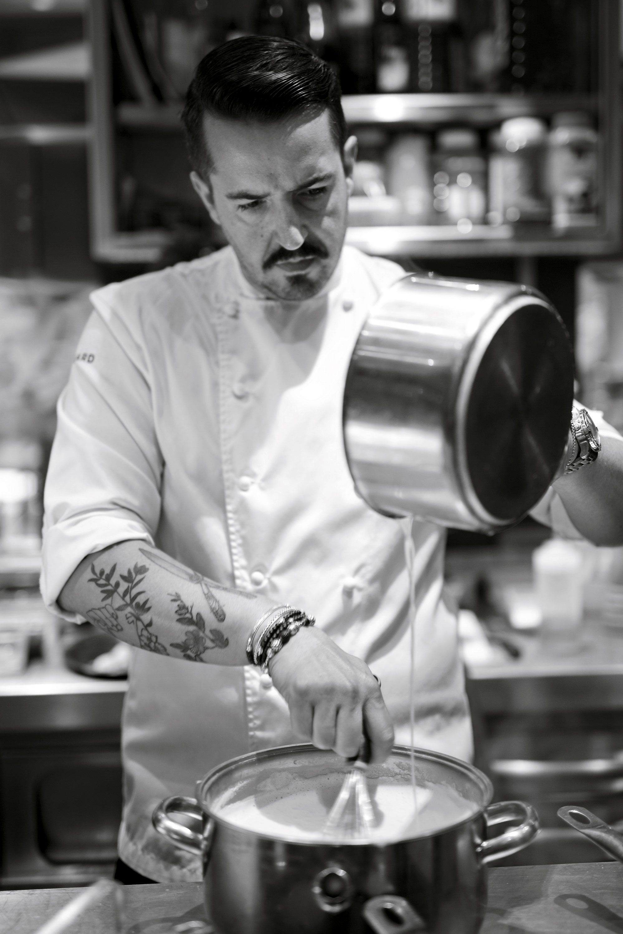 Le chef Olivier Da Silva en train de verser un mélange dans une casserole, la photo est en noir et blanc