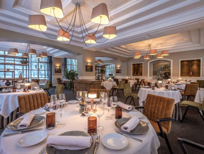 Salle de restaurant, lustre à 6 appliques, tables dressées dans les ton nappée blanc, vaisselle beige et blanche