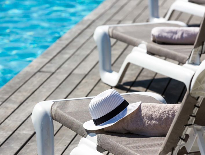 Détail de transat en bord de piscine avec canotier