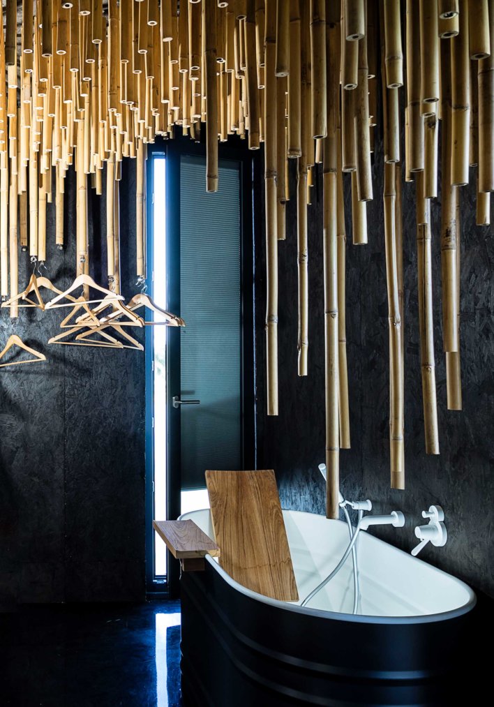Baignoire dans salle de bain design avec mur noir en ardoise et bambou suspendu au dessus