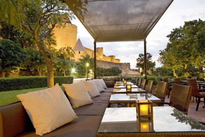 Un alignement de table en perspective. Sur les tables se trouvent des verres avec des chaises et des petits canapés avec des oreillers. Il y a un beau couché de soleil