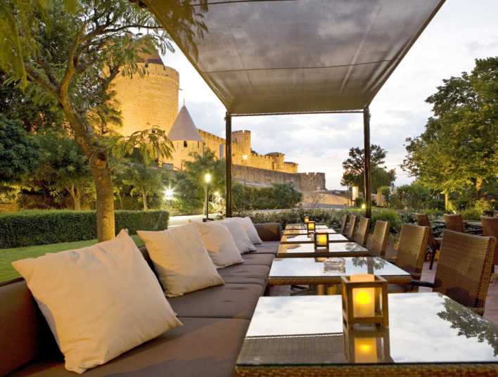 Un alignement de table en perspective. Sur les tables se trouvent des verres avec des chaises et des petits canapés avec des oreillers. Il y a un beau couché de soleil