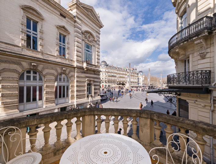 Terrasse où se trouve une table et des chaises blanches et la vue donne sur la place