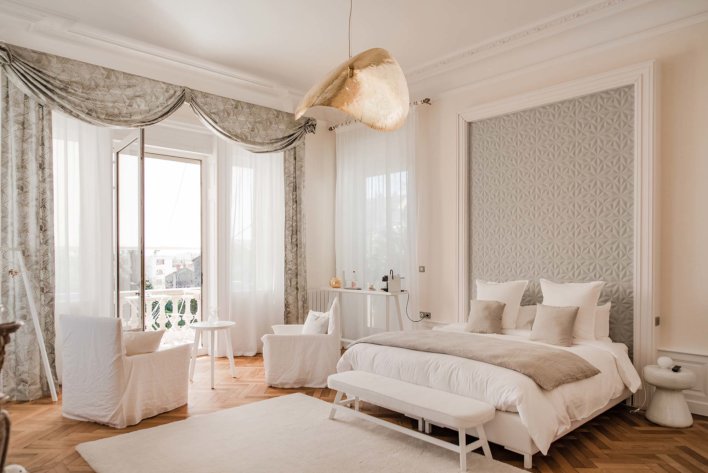 Grande chambre avec belle hauteur sous plafond, décoration dans les teintes de beige et de grisé, suspension et décoration design