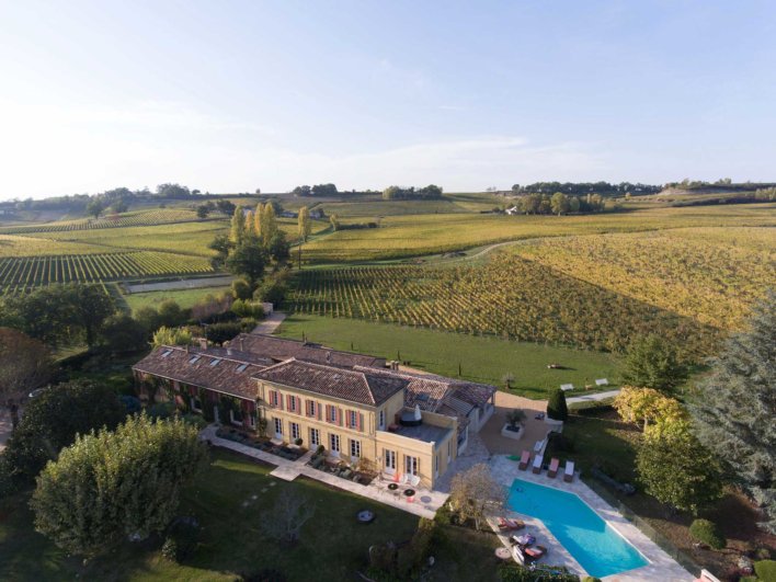 Vue aérienne d'une bâtisse typique du bordelais, avec vignes, coteaux et piscine extérieure