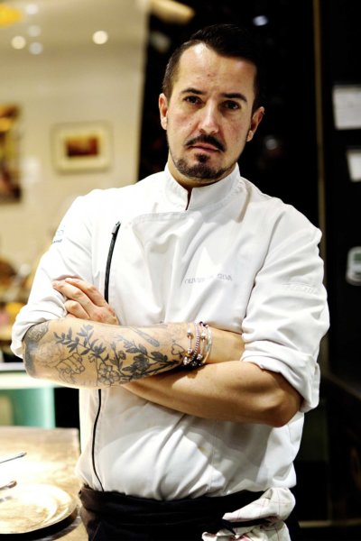 Portrait d'un chef en veste de cuisine blanche, quelques tatouages sur les bras,dans sa cuisine