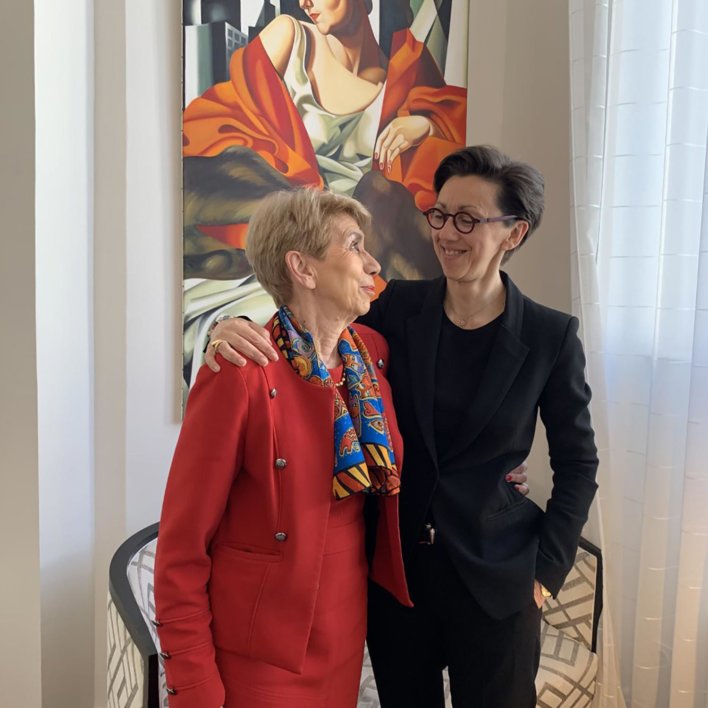 Deux femmes, une vêtue de rouge à gauche et l'autre vêtue de noir à droite, dans les bras l'une de l'autre, épaule contre épaule