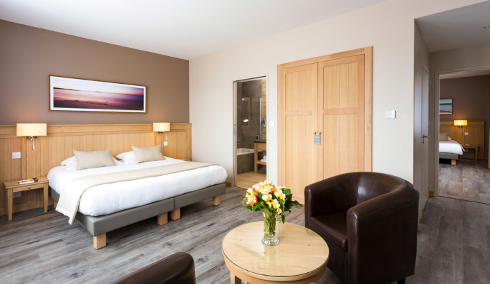 Chambre communicante spacieuse avec poster encadré représentant une plage lors d'un coucher de soleil, avec table basse et fauteuil en cuir.