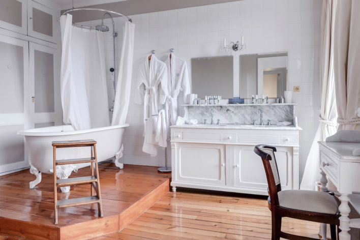 Grande salle de bain avec parquet au sol et baignoire vintage à pattes de lion.