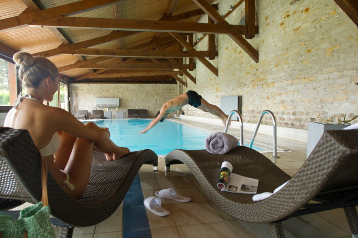 Jeune femme assise sur un transat pendant qu'un jeune homme effectue un plongeon dans la piscine.