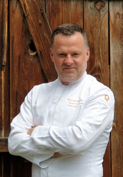 portrait de chef en veste blanche devant une porte en bois